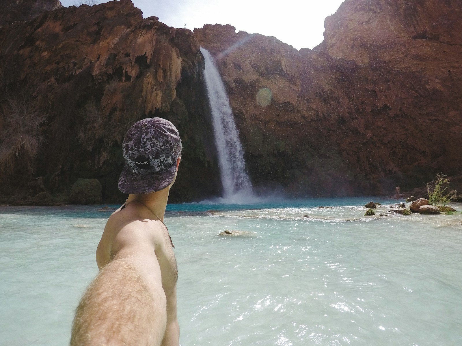 man in black cap sitting on rock in front of waterfalls during daytime